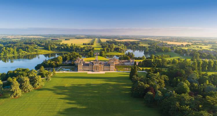 Drone view of Blenheim Palace and its vast landscaped parklands with reflective lakes and long tree avenues.
