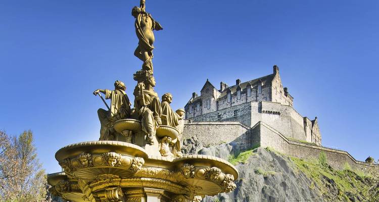 Victorian Ross Fountain with Edinburgh Castle perched on volcanic rock against a deep blue sky.
