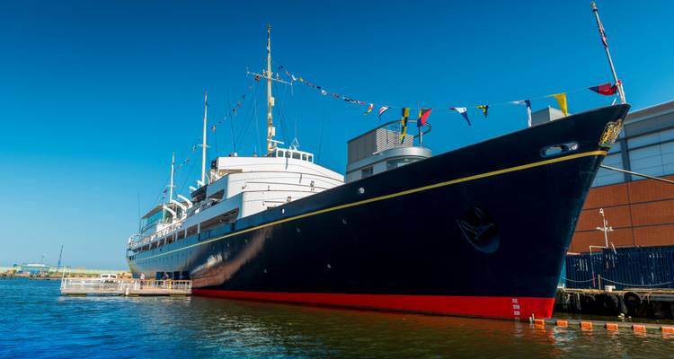The former Royal Yacht Britannia moored at Leith harbour decorated with nautical flags under clear sky.