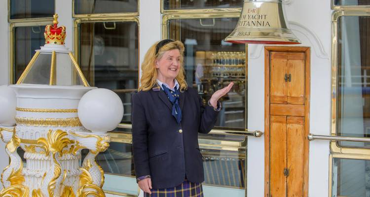 Guide in uniform gestures toward ship’s bell aboard Royal Yacht Britannia.
