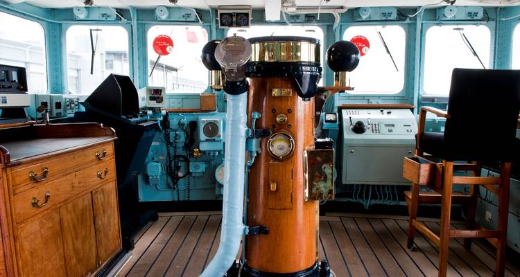 Vintage ship bridge interior with polished wooden compass stand and classic navigation equipment.
