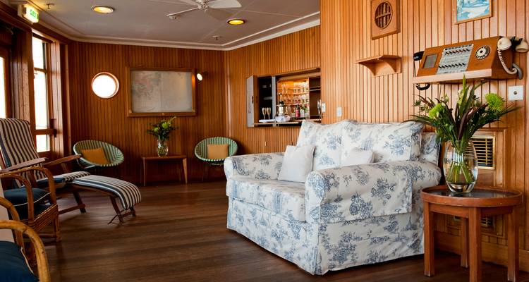 Cosy lounge aboard yacht with floral sofa, wooden panel walls and nautical decor.