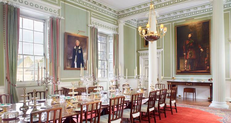 Stately dining room with pastel green walls, classical portraits and long table set with silverware in Scottish palace.