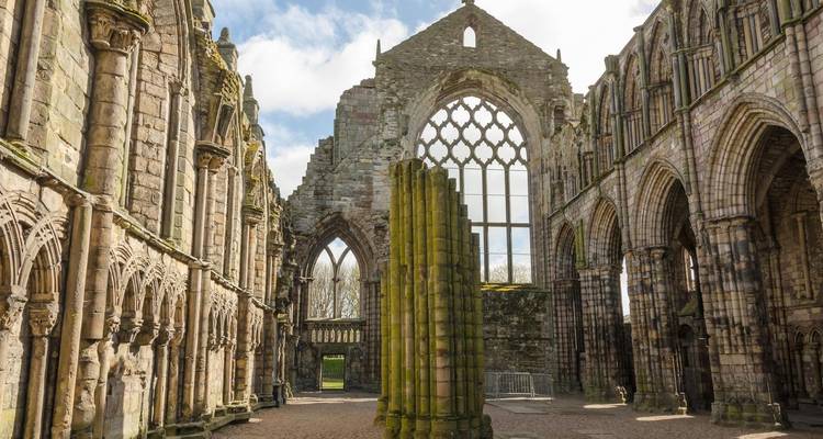 Atmospheric ruins of Holyrood Abbey with tall arched windows and mossy columns lit by soft daylight.