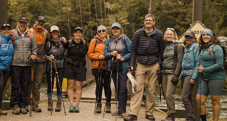 Un grand groupe de randonneurs posant avec des bâtons de trekking devant un pont suspendu en forêt.