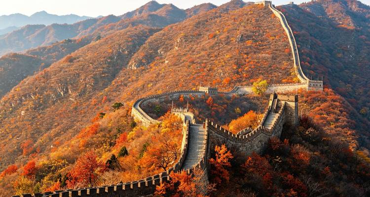 The Great Wall snakes across autumn-coloured mountain ridges under warm sunlight