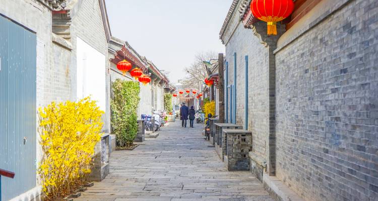 Narrow stone alley lined with gray brick walls and red lanterns with two people walking away