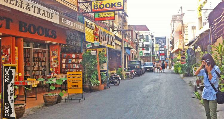 Une rue étroite et colorée à Chiang Mai bordée de librairies et de petits cafés, tandis qu'un voyageur prend des photos.