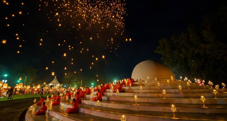 Des moines vêtus de robes orange sont assis sur de larges marches tandis que des centaines de lanternes illuminées par des bougies s'élèvent dans le ciel nocturne.