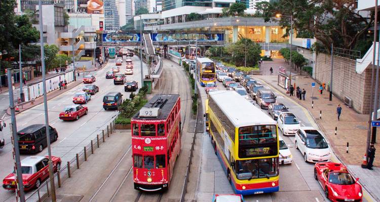 Busy Hong Kong street with iconic red tram, double-decker buses and traffic flanked by high-rise buildings.