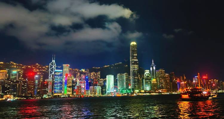 Night panorama of Hong Kong Island skyline with colorful lights reflecting on Victoria Harbour.