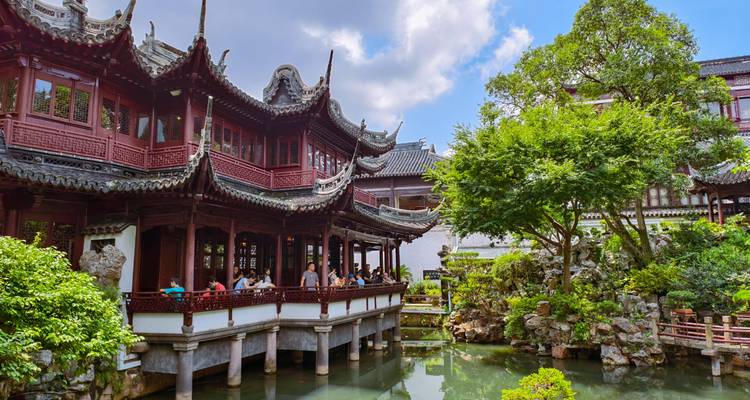 Classical Chinese garden in Shanghai with ornate wooden pavilions, rockeries and koi pond under sunny skies.