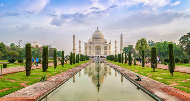 El icónico Taj Mahal reflejándose en el largo estanque central rodeado de jardines bien cuidados bajo un cielo pastel.
