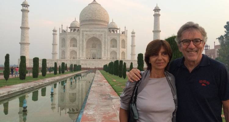 Pareja sonriente posando junto al estanque de reflejos frente al Taj Mahal al atardecer.