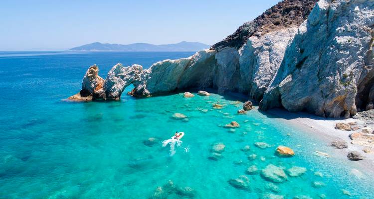Kristalhelder turquoise baai met een eenzame snorkelaar dicht bij dramatische witte kliffen en verspreide rotsen.