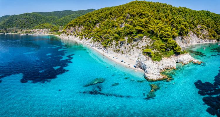 Helder turquoise water omzoomt een lange bosrijke kustlijn en een afgelegen wit zandstrand, gezien van bovenaf.