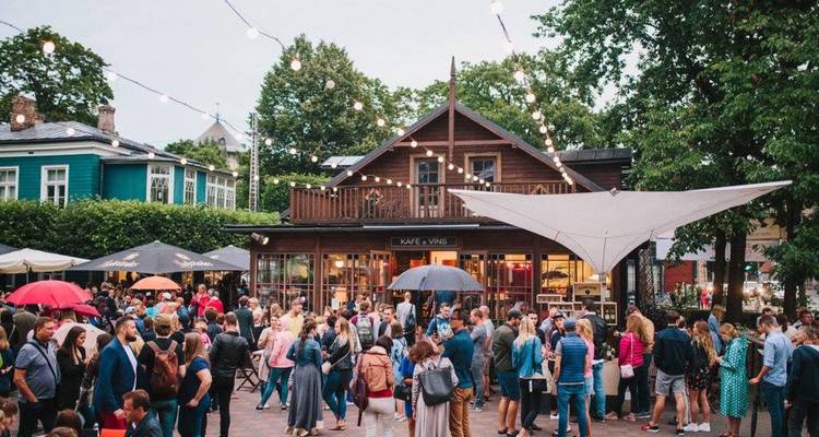 Marché extérieur animé ou festival avec des foules se rassemblant autour d'un café en bois sous des guirlandes lumineuses.