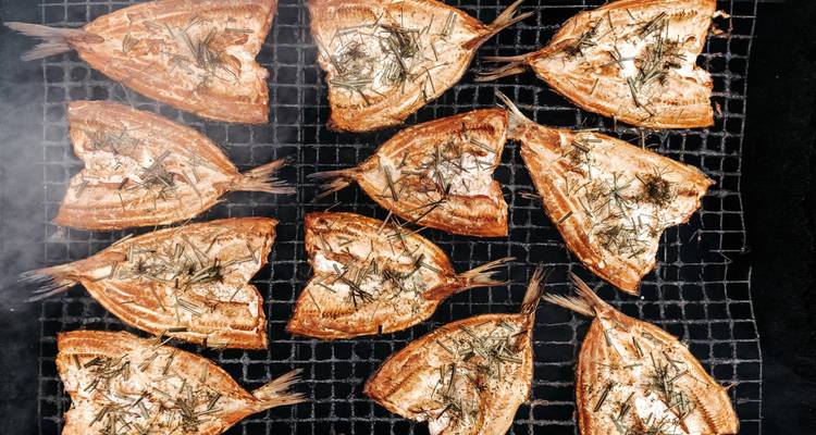 Vue aérienne de moitiés de poisson fumé disposées sur une grille de cuisson avec des herbes.