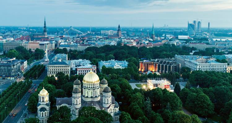 Panorama del atardecer del horizonte de Riga con torres de iglesias y parques verdes que desembocan en el río Daugava.
