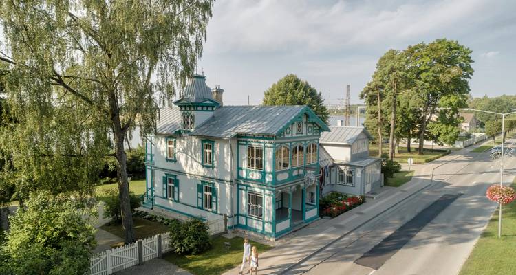 Vista de dron de una villa de madera decorativa pintada de color turquesa en una tranquila calle arbolada.