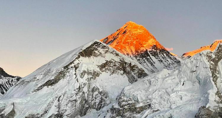 Le sommet du Mont Everest brillant d'une teinte orange au lever du soleil au-dessus de crêtes glacées et de glaciers.