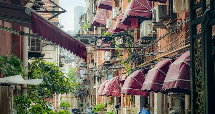 Smalle steeg in Shanghai met rode bakstenen shikumen-gebouwen, hangende luifels en in elkaar vervlochten draden boven je hoofd.