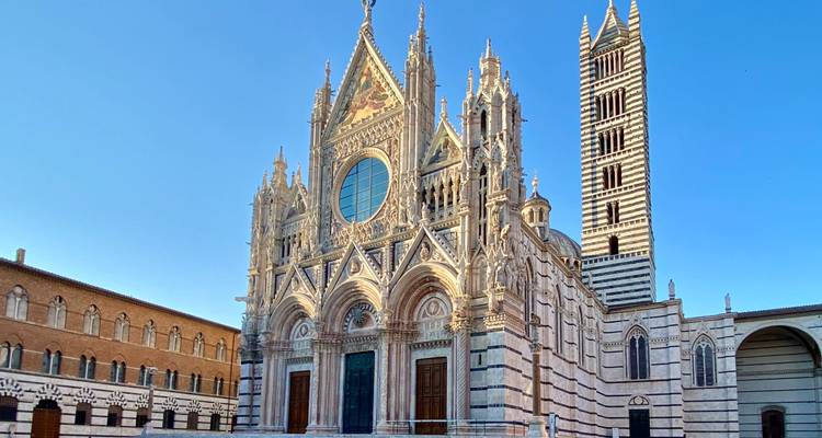 Magnífica fachada gótica de la Catedral de Siena brillando bajo el cielo azul despejado.