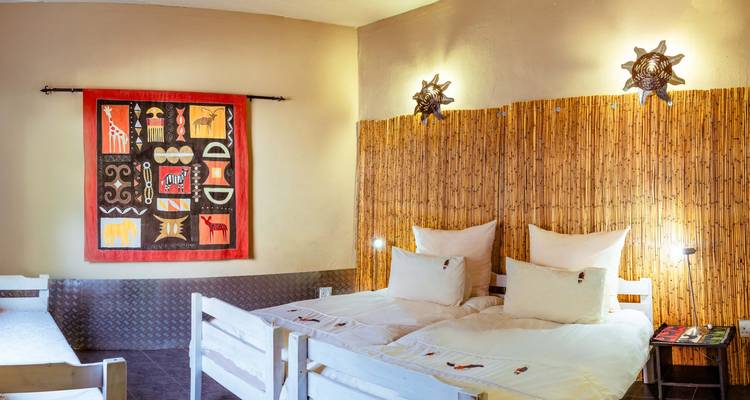 Brightly decorated lodge bedroom with twin beds, bamboo wall and African art