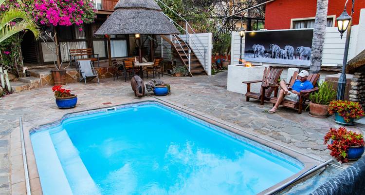 Cosy guesthouse courtyard with swimming pool, flowers and guest relaxing by outdoor fire