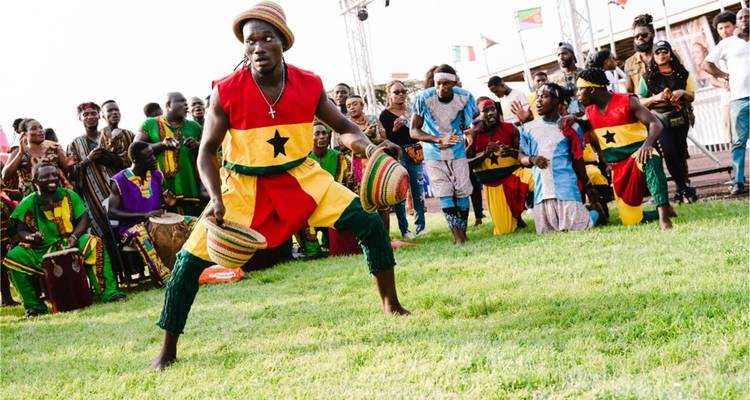 Troupe de danse culturelle dynamique en costumes ghanéens colorés se produisant sur un terrain herbeux.