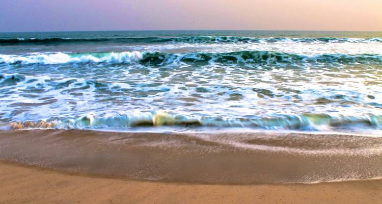Des vagues douces roulent sur une plage de sable sous un ciel pastel délicat au crépuscule.