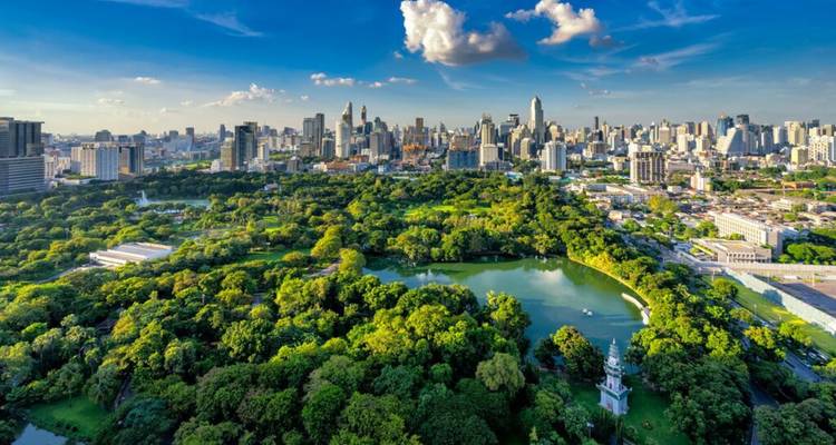 Parque urbano exuberante con lagos y árboles en medio de un horizonte moderno y expansivo bajo cielos azules y nubes esponjosas.