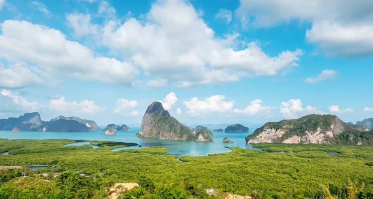 Islas de piedra caliza espectaculares se elevan desde aguas turquesas rodeadas por enormes bosques de manglares y cielo azul.
