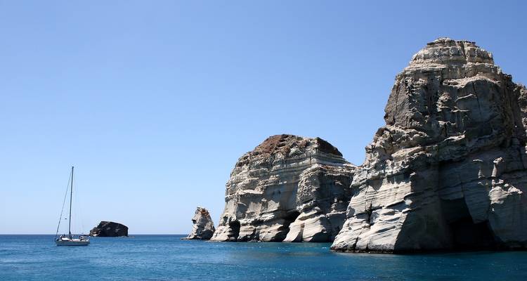 Des falaises maritimes blanc rayé s'élèvent majestueusement au-dessus d'eaux bleu profond tandis qu'un petit voilier dérive à proximité.