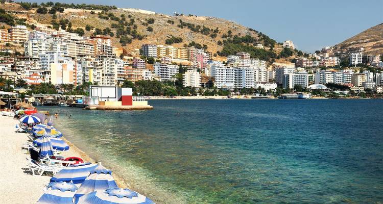 Los paraguas de colores y las tumbonas se alinean en la playa de guijarros frente a las aguas cristalinas de Saranda.