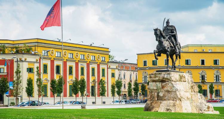 La estatua ecuestre de Skanderbeg domina la plaza principal de Tirana con edificios gubernamentales coloridos.
