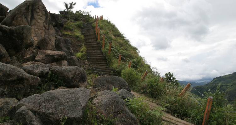 Empinados escalones de piedra en la ladera conducen hacia el arte rupestre tallado en la dirección de un horizonte andino nublado.
