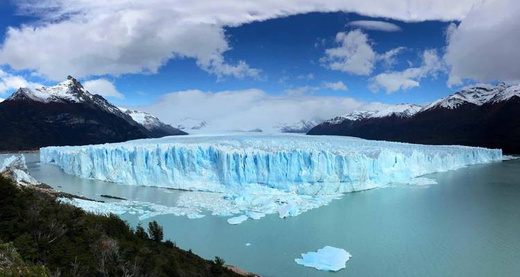 Panoramisch luchtfoto van Perito Moreno-gletsjer die zich uitstrekt over een turkooizen meer, omgeven door sneeuwbedekte bergen.
