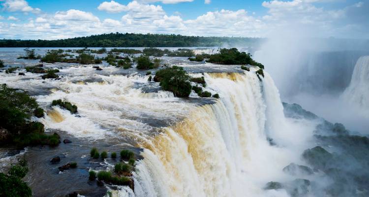 Zijkant van de Iguazu Falls met weelderige eilanden en opstijgende mist onder een heldere hemel.