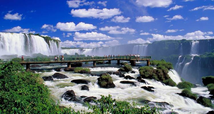 Loopbrug over de bruisende Iguazu waterval omgeven door een helder blauwe lucht en weelderig groen.
