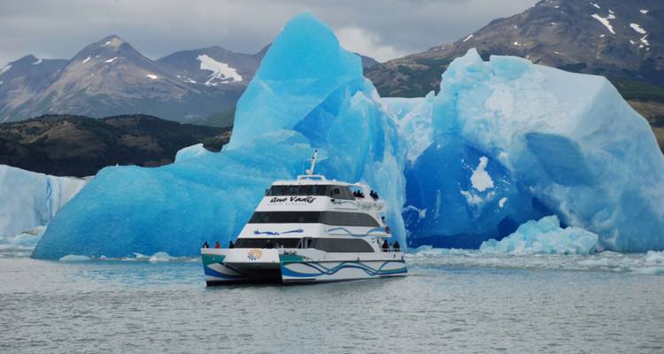 Rondvaarboot vaart langs imposante, schitterend blauwe ijsbergen met een bergachtergrond.