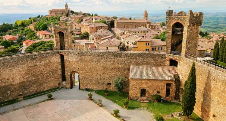 Una vista elevada de un pueblo medieval toscano fortificado rodeado de muros de piedra y tejados de terracota.