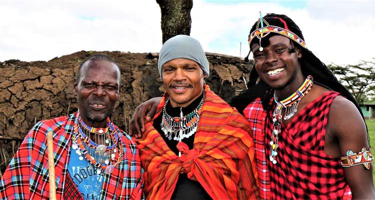 Tres hombres maasai en shuka rojo tradicional y abalorios posando juntos y sonriendo.