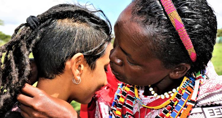 Primer plano de una mujer maasai tocando la cabeza de un viajero en un saludo tradicional.