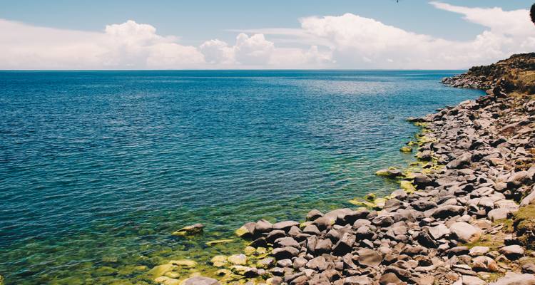 Les eaux turquoise cristallines viennent lécher le rivage rocheux du lac Titicaca sous un ciel brillant