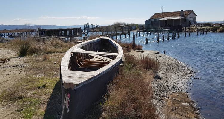 Un vieux bateau de pêche en bois repose sur le rivage d'un lagon de sable fin à côté de jetées en ruine sous un ciel dégagé.