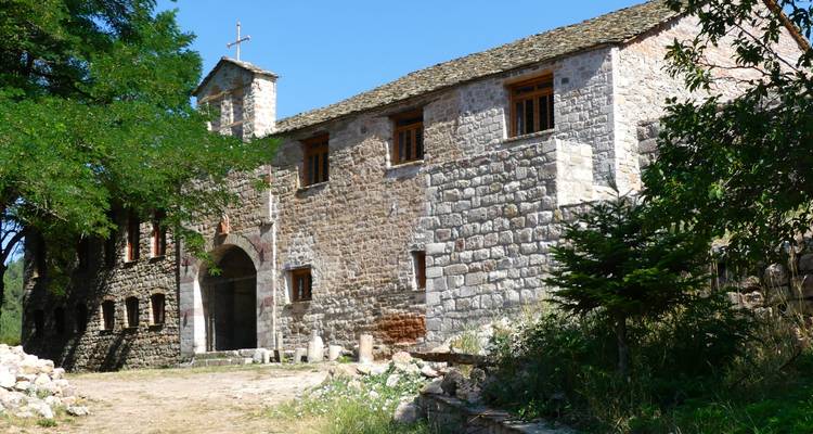Un monastère en pierre avec une entrée voûtée et des murs rustiques ombragés par des arbres feuillus en Albanie rurale.