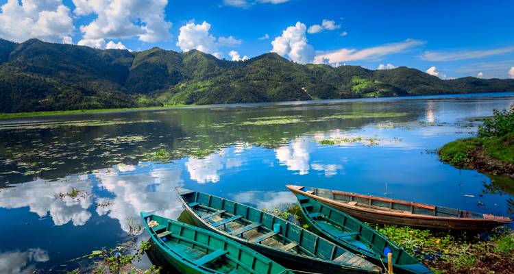 Colorful wooden boats float on the calm reflective waters of a mountain lake