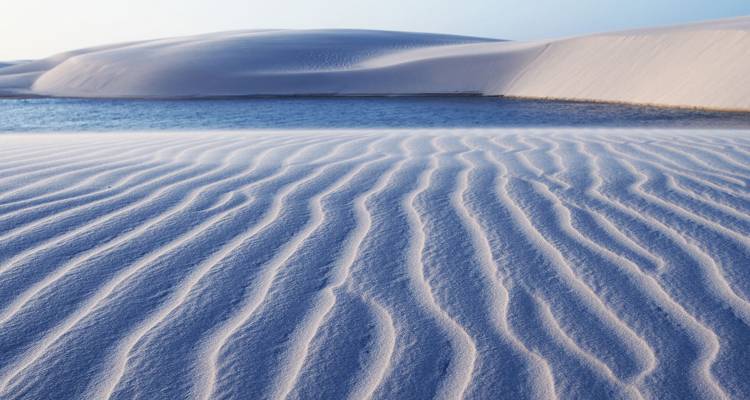 Rippled sand patterns leading to a blue lagoon and distant dune ridge at sunrise in Lençóis Maranhenses
