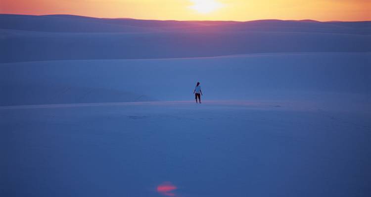 Lone traveller standing atop vast pastel-coloured dunes at sunset